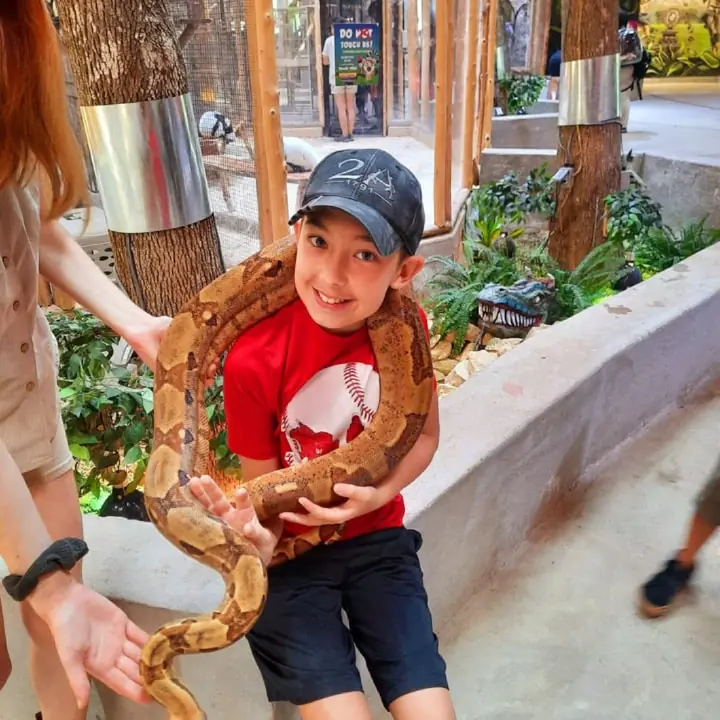 A grinning boy in a cap holding a large snake.